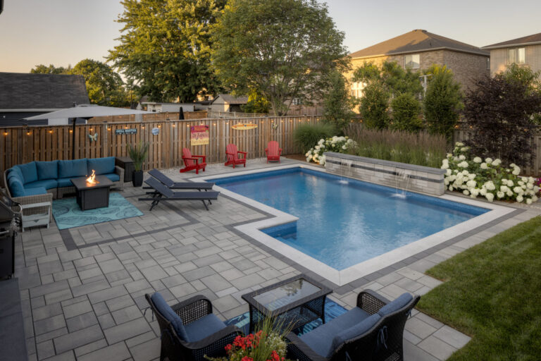 Backyard with a swimming pool, surrounded by patio furniture, plants, and a wooden fence. No people are present. A cozy, relaxing setting.