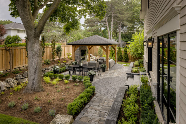 A well-landscaped backyard features a cozy gazebo, stone path, lush greenery, and wooden fencing, creating a serene outdoor living space.