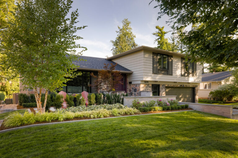 Modern suburban house with neatly landscaped yard, surrounded by trees. No people or recognizable landmarks are present. Peaceful, sunny atmosphere.