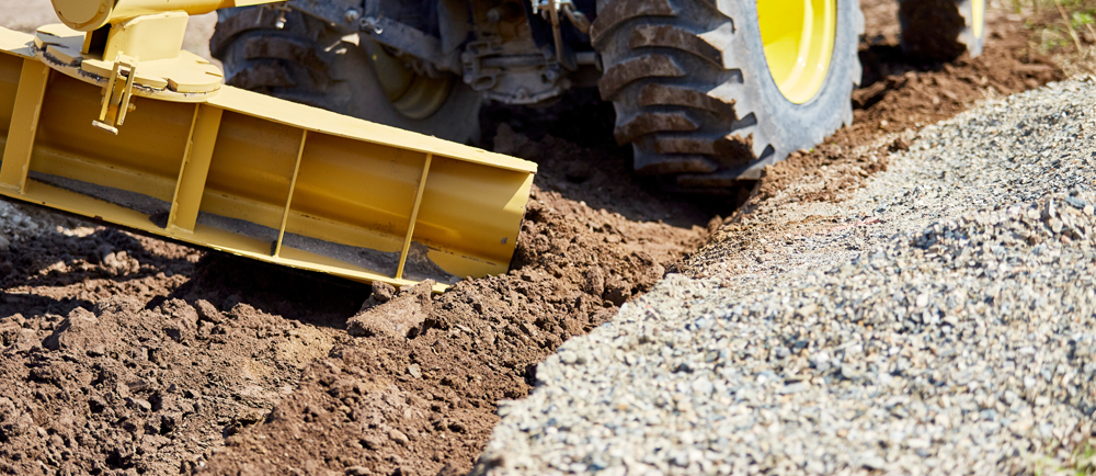 a machine pushing dirt along side gravel