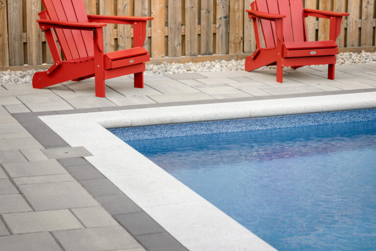 Two red chairs sit on a tiled patio by a swimming pool, with a wooden fence in the background. No people or landmarks visible.