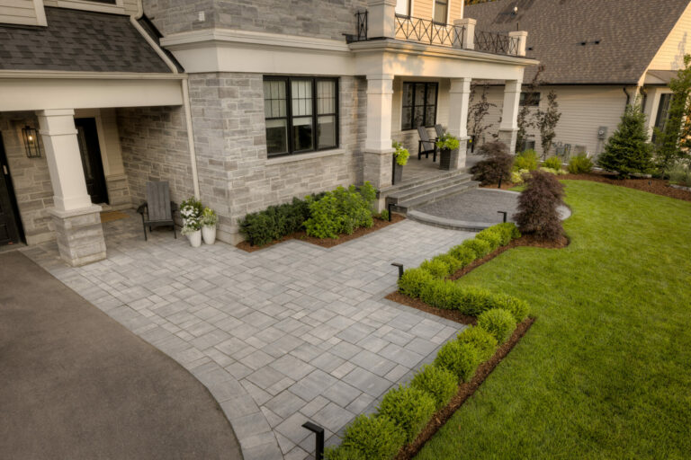 A stone house with a landscaped front yard, patio, and steps. Potted plants and shrubs accentuate the neat, modern design. No people present.