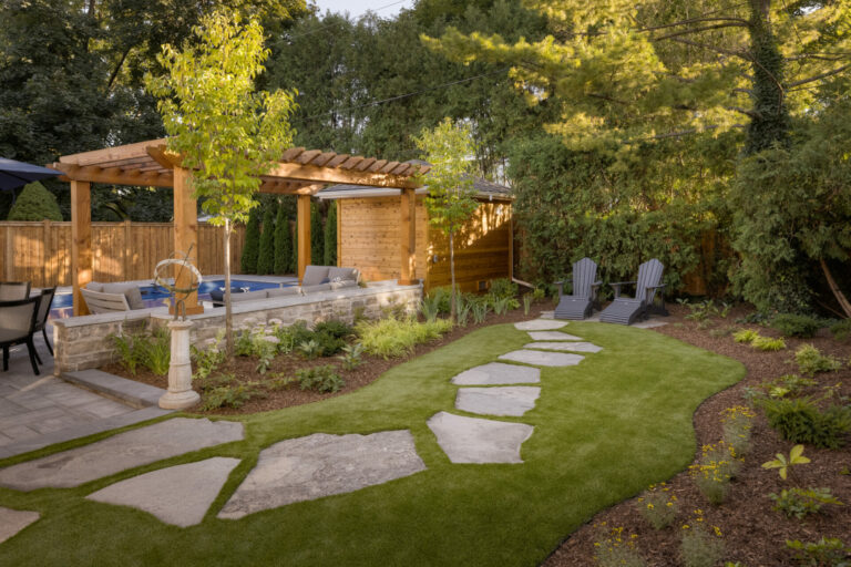 A tranquil backyard features a pergola, seating area, lush greenery, stone pathway, and Adirondack chairs amidst trees and shrubs.