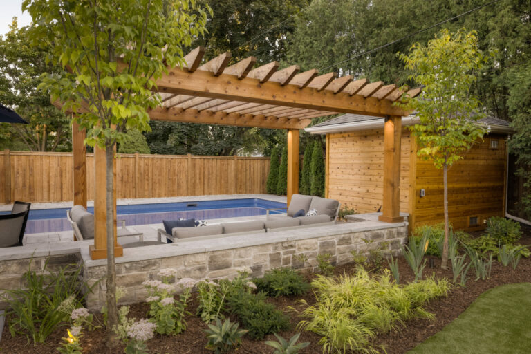 Backyard with wooden pergola over a modern pool, surrounded by lush greenery and a wooden fence, creating a serene outdoor lounging area.