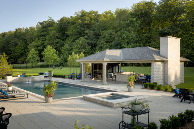 A serene backyard scene with a modern poolside pavilion, seating areas, surrounded by lush green trees and manicured lawn. No people present.