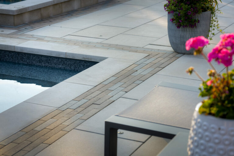 A serene poolside area with elegant paving, colorful flowers in planters, and a tranquil atmosphere, inviting relaxation and leisure.