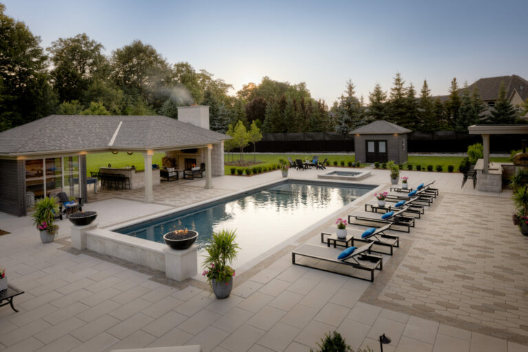 A luxurious backyard features a modern swimming pool, lounge chairs, and a gazebo surrounded by lush greenery at sunset.