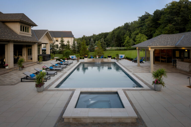 Luxurious backyard with a rectangular pool, surrounded by lounge chairs, modern houses, and lush greenery. Peaceful, spacious outdoor setting for relaxation.