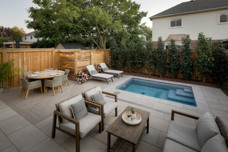 A cozy backyard patio features seating, a dining set, and a small pool, surrounded by plants and a wooden fence on a sunny day.